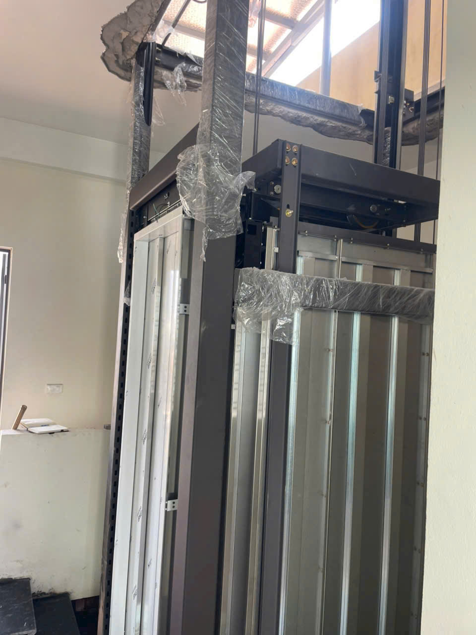 Thang máy gia đình đang lắp đặt với khung kim loại và cửa tầng bọc nilon bảo vệ